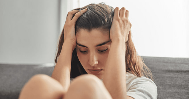 Anger-and-Anxiety A woman sitting leaning to a sofa with her both hands on the head