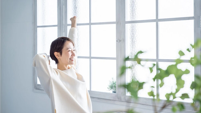 a-woman-dressed-in-white-stretching-and-smiling-in-front-of-a-large-window a-woman-dressed-in-white-stretching-and-smiling-in-front-of-a-large-window