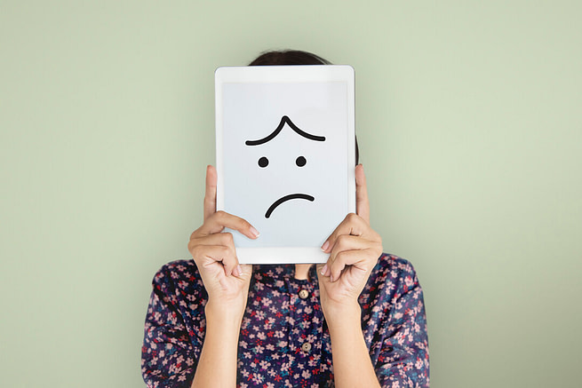 1643712396803 A woman hiding her face with a paper having sad emoji