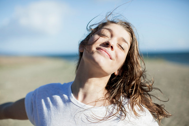 Young woman with eyes closed smiling on a beach Hair in the wind, she takes advantage of beams of the sun