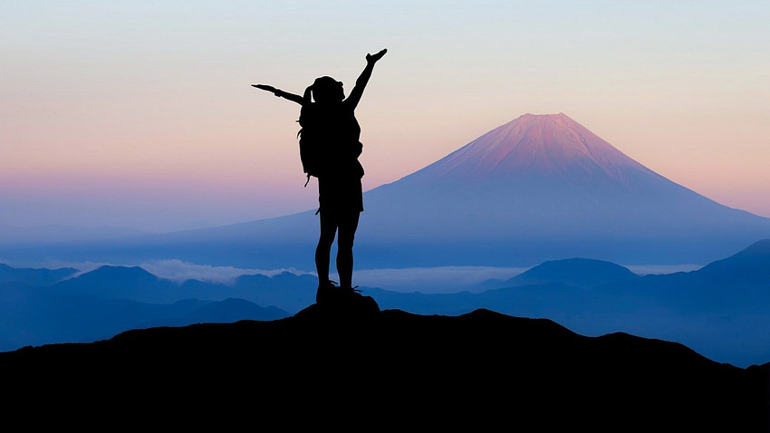 A woman on the top of a mountain with her hands raised for clarity of mind